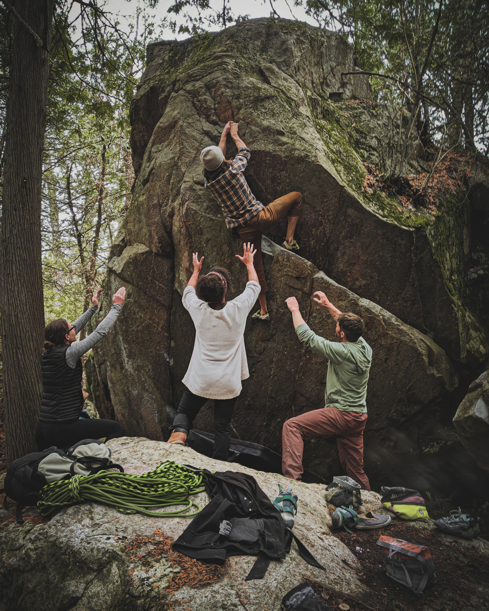 Boulderers spotting a climber on a natural rock in the forest